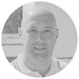 Carlos García Torrijos, un hombre con la cabeza rapada, sonríe ligeramente a la cámara. Lleva una camisa con cuello y está fotografiado en blanco y negro, con un borde circular alrededor de la imagen.