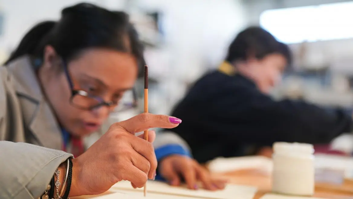 Una persona con un pincel parece estar pintando sobre papel, mientras otra trabaja en una mesa de un aula o estudio de arte. Los materiales artísticos son visibles, lo que refleja cómo los talleres creativos pueden ser beneficiosos para las personas con discapacidad en la Comunidad de Madrid. Una persona con un pincel parece estar pintando sobre papel, mientras otra trabaja en una mesa de un aula o estudio de arte. Los materiales artísticos son visibles, lo que refleja cómo los talleres creativos pueden ser beneficiosos para las personas con discapacidad en la Comunidad de Madrid.