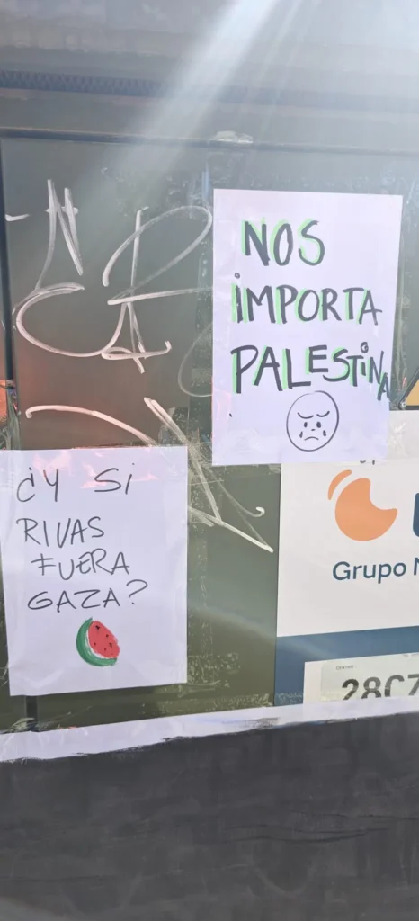 En una pared hay pegados dos carteles escritos a mano por madres y padres del CEIPSO La Luna. Uno dice ¿Y si Rivas fuera Gaza? con un dibujo de una sandía; el otro dice Nos importa Palestina, junto a una cara triste y unas banderas palestinas.