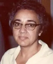 Una persona con pelo corto rizado y canoso y gafas, que recuerda a la matemática española MARÍA WONENBURGER, lleva una camisa de cuello claro y mira a la cámara con expresión neutra. El fondo está desenfocado.