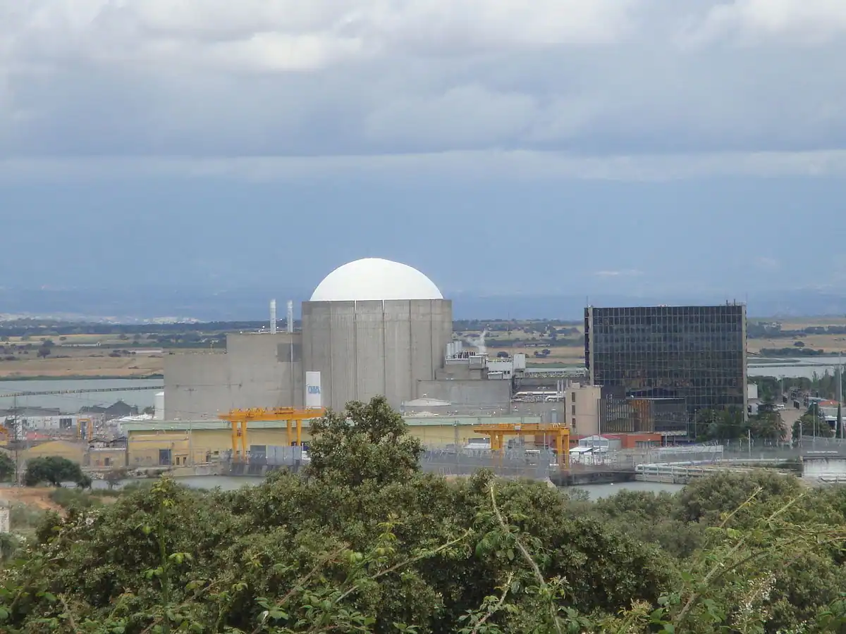 Una central nuclear con un gran edificio de contención en forma de cúpula blanca se alza entre arbustos y campos bajo un cielo nublado, mientras los ecologistas en acción expresan su preocupación por su impacto en el paisaje rural. Una central nuclear con un gran edificio de contención en forma de cúpula blanca se alza entre arbustos y campos bajo un cielo nublado, mientras los ecologistas en acción expresan su preocupación por su impacto en el paisaje rural.