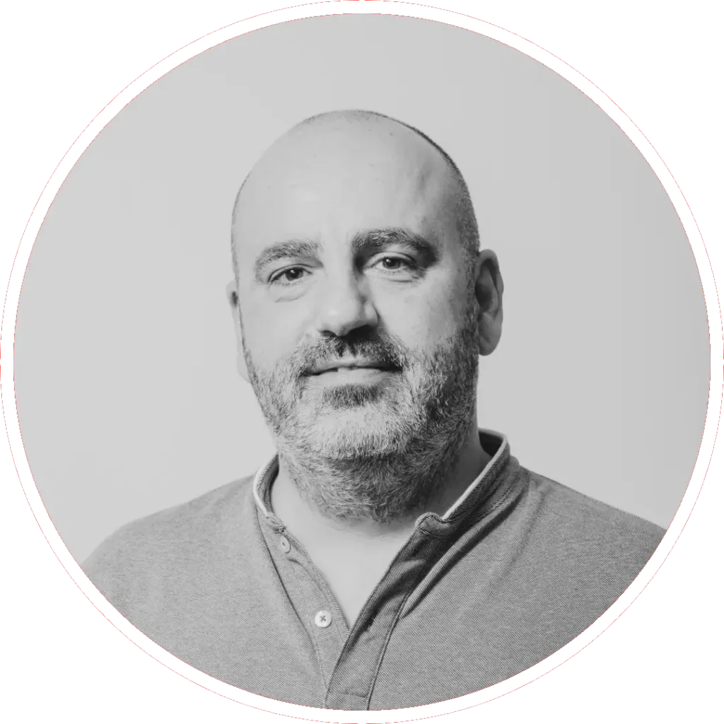 Un hombre de mediana edad, con la cabeza y la barba afeitadas y vestido con camisa de cuello, mira a la cámara con expresión neutra. La imagen en blanco y negro de Adolfo Calle está enmarcada por un borde circular.