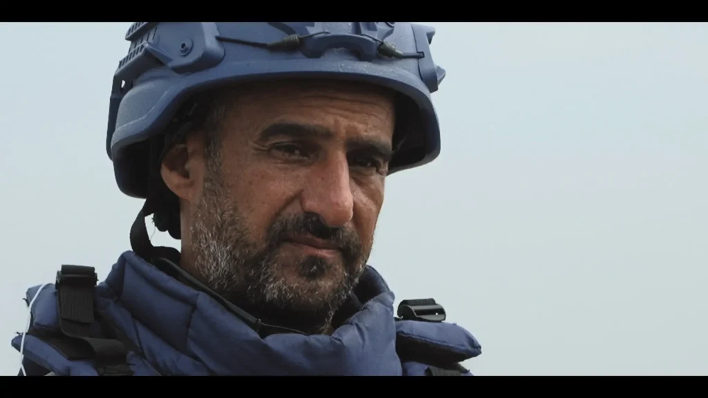 Un hombre con barba y bigote lleva un casco azul y un chaleco protector, y mira ligeramente hacia un lado. El fondo liso evoca el tono serio que suele verse en un acto de Derechos Humanos o en el Festival de Cine de Madrid.