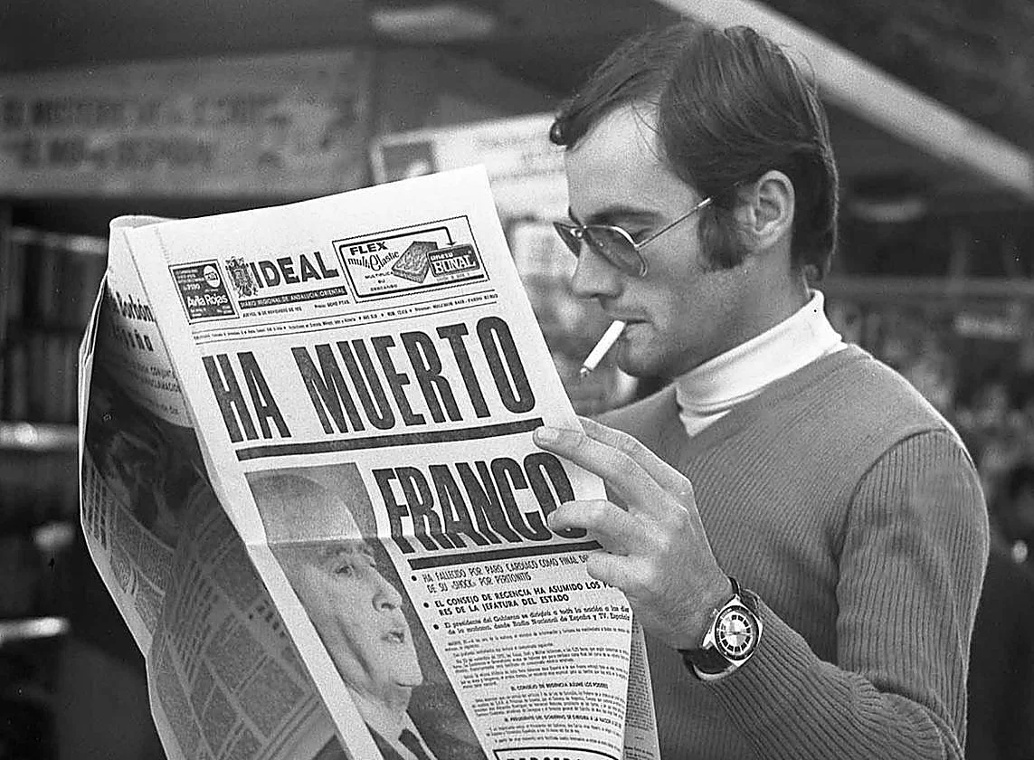 Un hombre con gafas de sol y jersey fuma un cigarrillo mientras lee un periódico con el titular «HA MUERTO FRANCO» y una foto en blanco y negro de Franco en portada, reflexionando sobre las polémicas inmatriculaciones. Un hombre con gafas de sol y jersey fuma un cigarrillo mientras lee un periódico con el titular "HA MUERTO FRANCO" y una foto en blanco y negro de Franco en portada, reflexionando sobre las polémicas inmatriculaciones.