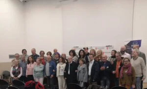 Un grupo de unos 30 adultos, hombres y mujeres, posan juntos en varias filas dentro de una sala con paredes blancas durante el Encuentro de Poetas en Red en Rivas. Al fondo se ven pancartas y sillas vacías.