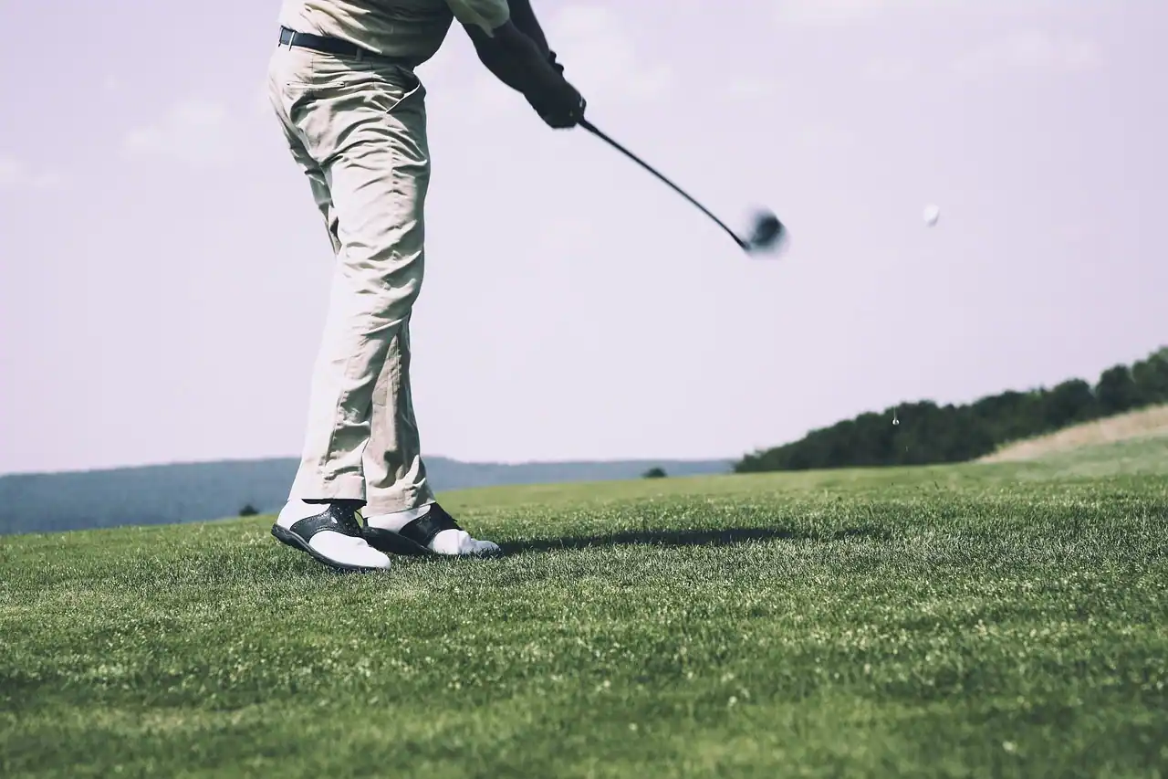 Una persona vestida con pantalones claros y camiseta de manga larga golpea un palo de golf en el campo de golf de La Moraleja. La pelota de golf está en el aire y solo se ve la mitad inferior del cuerpo de la persona. Una persona vestida con pantalones claros y camiseta de manga larga golpea un palo de golf en el campo de golf de La Moraleja. La pelota de golf está en el aire y solo se ve la mitad inferior del cuerpo de la persona.