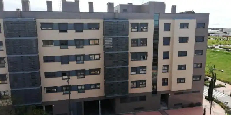 Un moderno edificio de apartamentos de varias plantas con paredes exteriores de color beige y gris, numerosas ventanas y algunos balcones refleja el cambiante horizonte de España a medida que crece la preocupación por los hogares hacinados en toda la UE. Al fondo se ve vegetación.