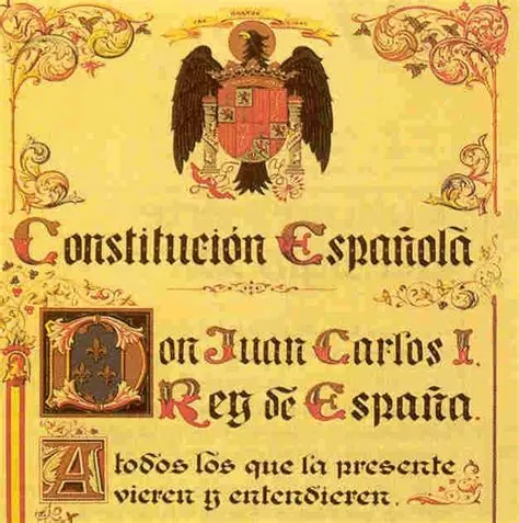 Una página decorativa con texto ornamentado y un escudo real en la parte superior, titulada «Constitución Española», en referencia al rey Juan Carlos I de España, destaca el marco constitucional y presenta una caligrafía y unos bordes elaborados. Una página decorativa con texto ornamentado y un escudo real en la parte superior, titulada "Constitución Española", en referencia al rey Juan Carlos I de España, destaca el marco constitucional y presenta una caligrafía y unos bordes elaborados.