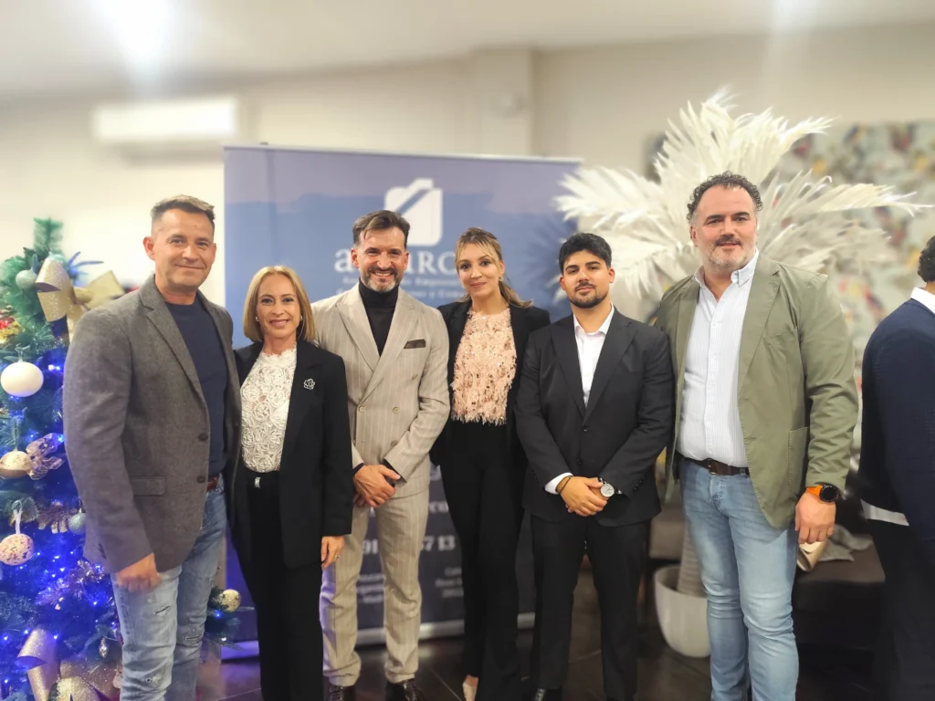 Seis empresarios sonríen para una foto de grupo en un encuentro navideño. Detrás de ellos hay una pancarta azul de ASEARCO y un árbol blanco decorativo, con un árbol de Navidad decorado parcialmente visible a la izquierda.