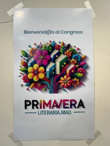 Un cartel pegado en una pared reza Bienvenid@s al Congreso Primavera Literaria.MAD. y muestra coloridas flores y libros, resaltando el vibrante espíritu del Congreso Primavera Literaria de Rivas.