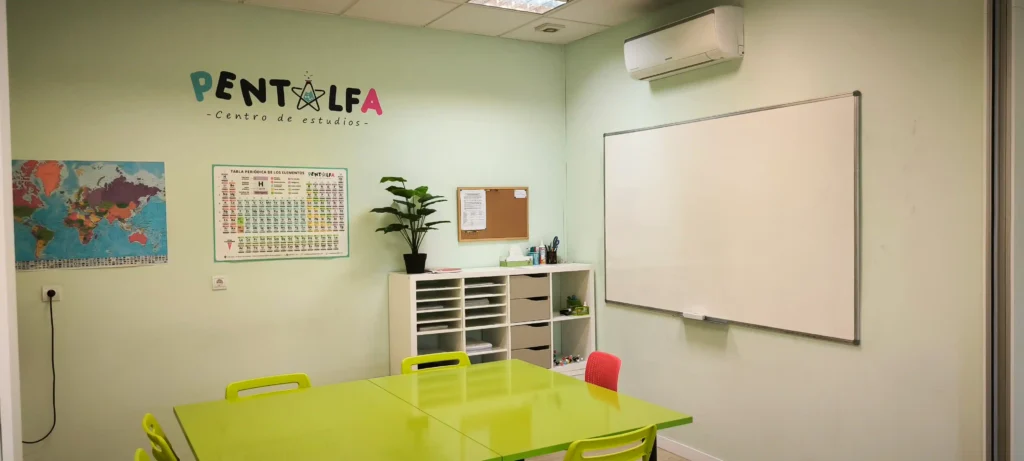 Un aula de la academia Pentalfa tiene paredes verde pálido, una mesa verde lima con sillas, una pizarra blanca, una tabla periódica, un mapamundi, una planta, estanterías con material y un tablón de anuncios, ideal para el aprendizaje escolar. "PENTALFA" está pintado en la pared.