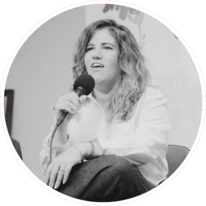 Yolanda Hidalgo es una mujer con el pelo ondulado está sentada sosteniendo un micrófono, lleva una camisa de color claro y pantalones oscuros. Parece estar hablando o respondiendo a preguntas en un debate. La imagen es en blanco y negro.