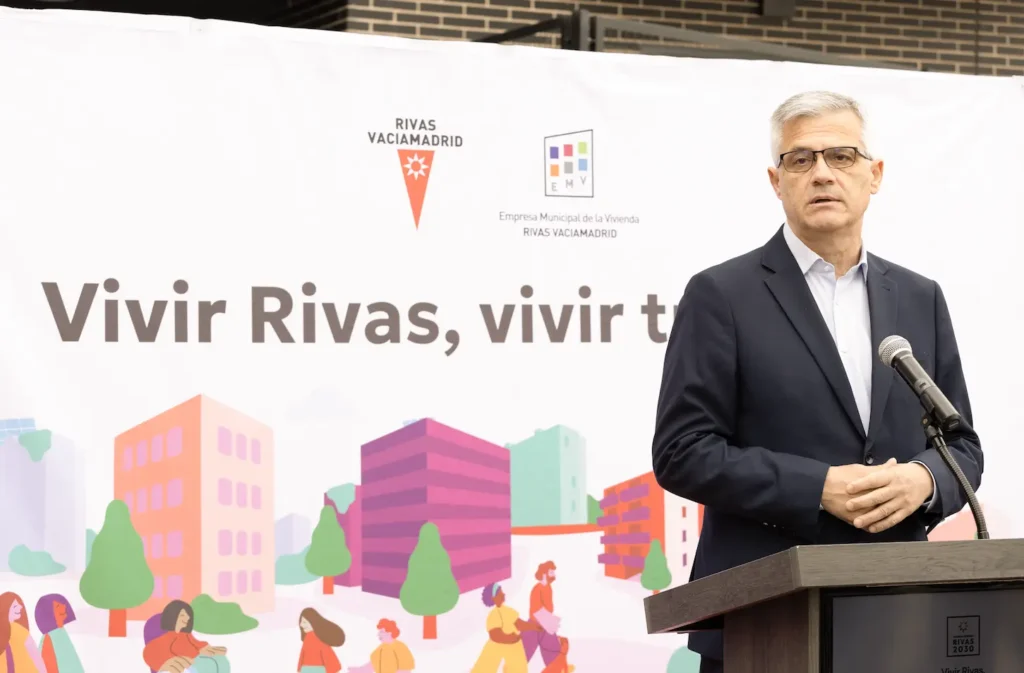 Un hombre con gafas y traje oscuro habla en una tribuna en Rivas, delante de una pancarta en la que se lee