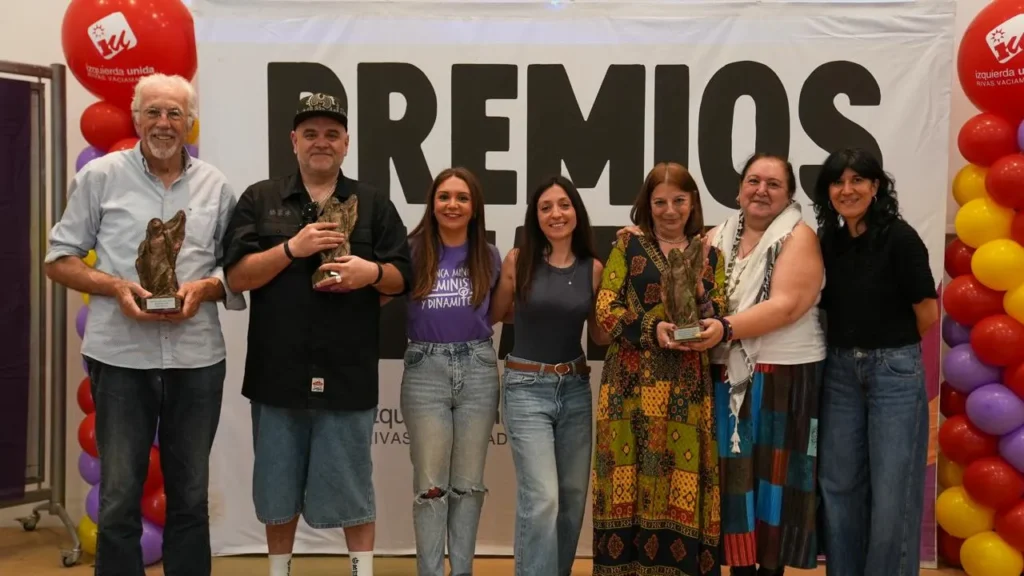 Siete personas de pie delante de una pancarta en la que se lee PREMIOS en las Jornadas Republicanas de Rivas. Algunos sostienen trofeos y a ambos lados hay globos de colores. Sonríen y posan para la foto.