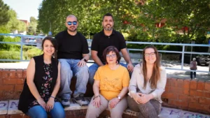 Cinco adultos se sientan en unas escaleras de ladrillo al aire libre en Covibar, posando para una foto de grupo. Los árboles y la vegetación llenan el fondo, con un niño pequeño en la distancia, capturando un momento comunitario que refleja las mejoras en el barrio.