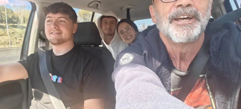Cuatro personas están sentadas dentro de un coche, capturando recuerdos mientras el pasajero delantero se toma un selfie. El conductor, con una camiseta negra, y dos amigos sonrientes en la parte trasera crean un momento alegre de camino a explorar Hong Kong.