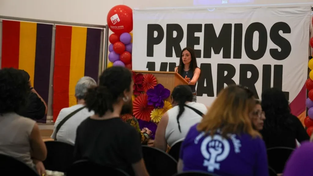 Una mujer habla en un podio frente a un gran cartel de los Premios 14 Abril durante las Jornadas Republicanas de Rivas. Unas 500 personas escuchan sentadas, rodeadas de globos rojos, amarillos y morados y flores.