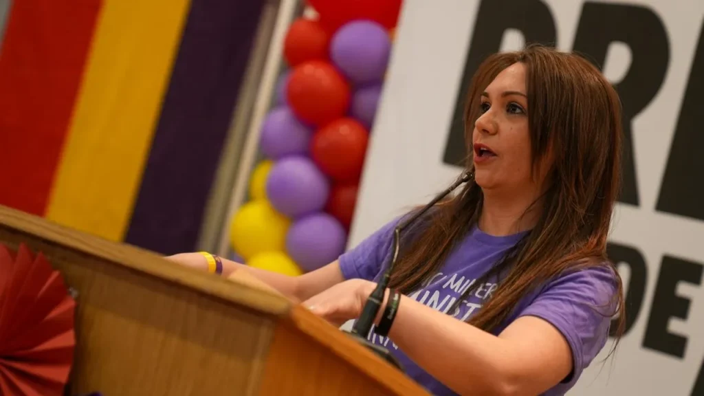 Aída Castillejo, alcaldesa de Rivas y coordinadora local de IU, habla en un podio de madera, con una camisa morada. Al fondo se ven globos de colores y un gran cartel que hace referencia a las Jornadas Republicanas y los Premios 14 de Abril.