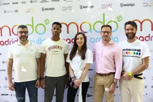 Cinco personas posan en fila delante de un telón de fondo con los logotipos de «Mado Madrid Orgullo» y «Orgullo 2026». Cuatro hombres y una mujer miran a la cámara, todos sonrientes, mientras las pancartas de los patrocinadores resaltan el apoyo contra la lgtbifobia.