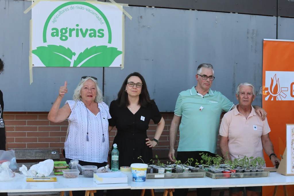 Cuatro personas de pie detrás de una mesa con plantones y pequeñas plantas en macetas en la fiesta de las asociaciones de Rivas, contando lo que hace Agrivas.