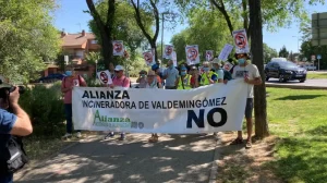 Un grupo de personas de pie en una acera de Rivas, sosteniendo carteles con el símbolo "no" y una pancarta en la que se lee "Alianza Incineradora de Valdemingómez NO", exigiendo el cierre de Valdemingómez. Al fondo aparecen árboles y casas.