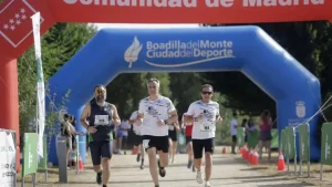 Tres hombres corren hacia la línea de meta en una carrera al aire libre que se celebra en Arco Verde, pasando por debajo de un arco hinchable azul y una pancarta roja. Este recorrido panorámico tiene una longitud de 222 kilómetros y conecta 25 municipios de la Comunidad de Madrid.