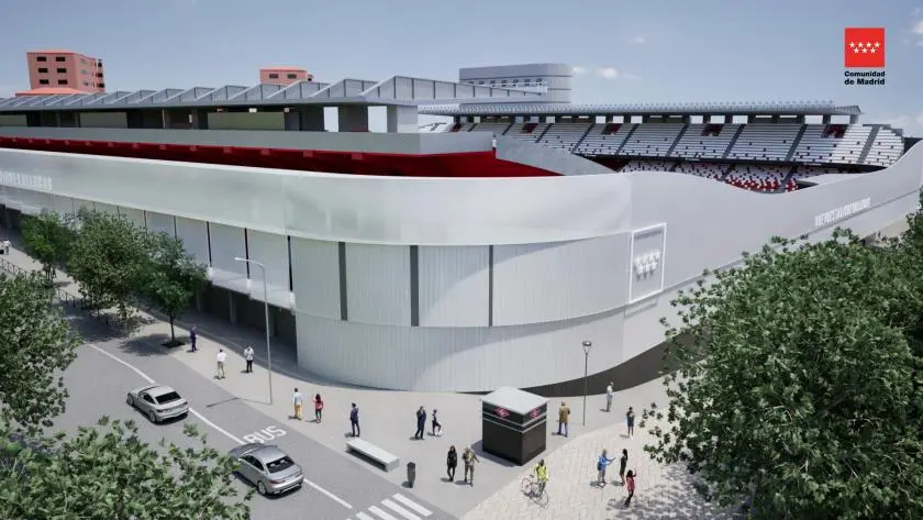 Un moderno Estadio de Vallecas con paredes exteriores blancas y curvas, detalles en rojo y un techo abierto. Se ve a los espectadores en el interior. La gente camina por las calles arboladas de los alrededores. Al fondo se divisan los edificios rojos y blancos de la Comunidad.