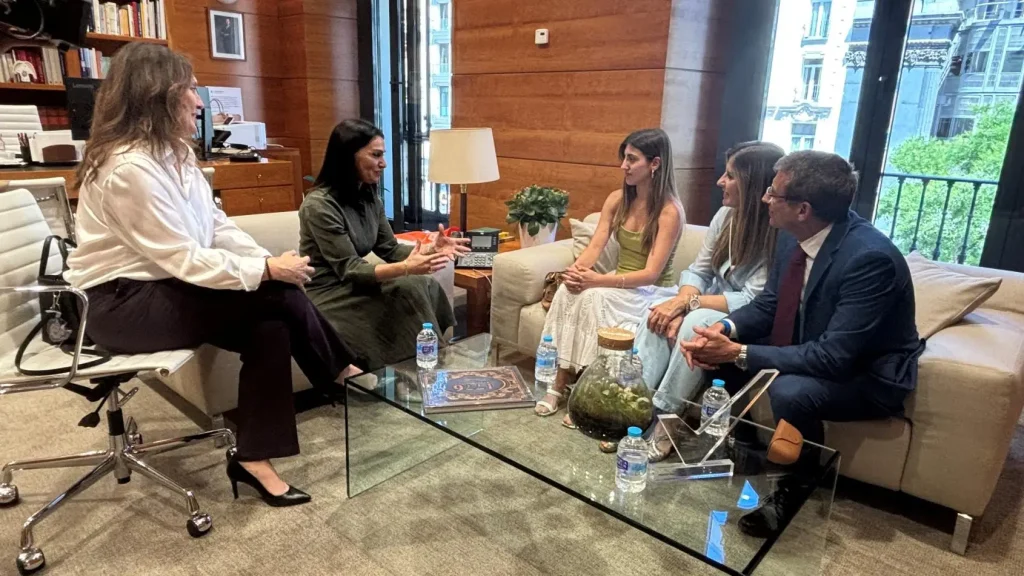 Cinco personas están sentadas charlando en una moderna oficina de Madrid, con paredes revestidas de madera y grandes ventanales, hablando de la mejor nota en el PAU. Están reunidas alrededor de una mesa de centro de cristal en la que hay botellas de agua, un terrario y libros. Al fondo se ven unas estanterías y una lámpara.