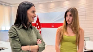 Dos mujeres están de pie en el interior de una habitación, conversando. Una de ellas, Valeria Fragola, de pelo oscuro y camiseta verde, tiene los brazos cruzados; la otra tiene el pelo largo castaño claro y lleva un vestido sin mangas de color verde claro. Al fondo se ve una bandera de la PAU de Madrid.