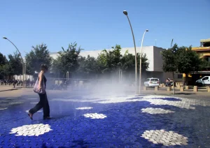 Una mujer cruza por una instalación de chorros de agua en una plaza | Foto de 123RF/fotovlad