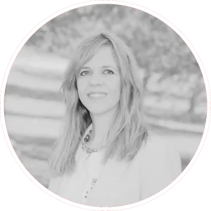 Concejala del PP de Rivas. Leticia Panadero Sáez, una mujer de pelo largo que lleva una chaqueta de color claro y un collar, está de pie al aire libre. Sonríe y mira a la cámara. La foto es en blanco y negro, con un fondo natural desenfocado.