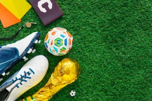Equipamiento de fútbol para jugar sobre césped, que incluye botas blancas con tacos, un silbato, tarjetas rojas y amarillas, un bloc de notas, un balón de fútbol de colores, un balón de fútbol pequeño y un trofeo dorado que se asemeja a la Copa del Mundo de la FIFA: perfecto para celebrar la pasión de España por el Mundial de Fútbol o para ver el gran partido en una pantalla gigante.