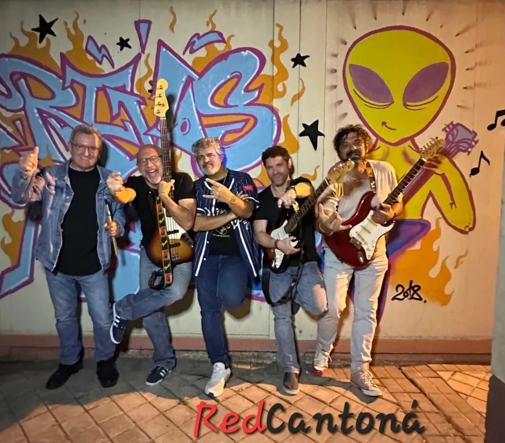 Cinco hombres posan con guitarras, una batería y conos de helado delante de un muro cubierto de grafitis con motivos muy llamativos y una gran figura de un extraterrestre amarillo. La palabra «RedCantoná» aparece en la parte inferior, en letras gruesas de color rojo y negro. Uno de los hombres, Juan, destaca entre el grupo.