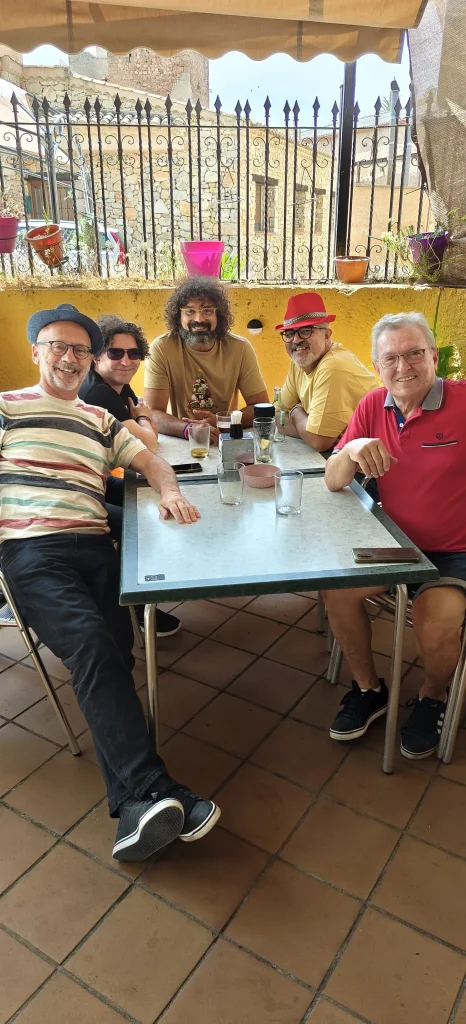 Cinco personas, miembros del «grupo ripense», están sentadas alrededor de una mesa en un restaurante al aire libre, todas sonriendo a la cámara. Hay bebidas sobre la mesa, plantas en macetas en una repisa detrás de ellas y una valla metálica al fondo. Entre ellas se encuentra Juan, de RedCantoná, que contribuye al ambiente alegre de esta reunión tan cordial.