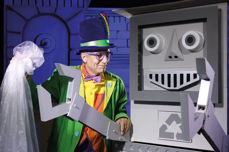 Una persona con un traje colorido y un sombrero de copa está de pie junto a un gran robot gris con brazos en forma de pinza y el símbolo de reciclaje, y sostiene una bolsa de plástico. El fondo presenta motivos geométricos iluminados en azul, lo que crea una escena llena de energía del Festival de Cultura en la Calle 2026.