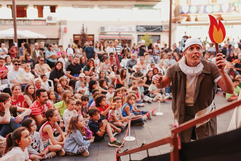 Un artista disfrazado sostiene una antorcha de atrezo y entretiene a una gran multitud de adultos y niños sentados en un acto al aire libre durante el día, cautivando al público en el Festival de Cultura en la Calle 2026.