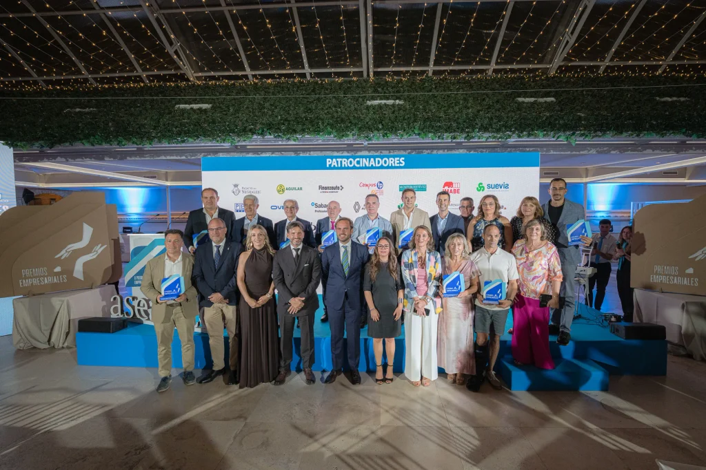 Un grupo de personas vestidas de gala posa en un escenario durante la ceremonia de entrega de los Premios Empresariales de ASEARCO. En el telón de fondo se ven los logotipos de los patrocinadores, y algunas personas sostienen placas conmemorativas. El escenario cuenta con iluminación decorativa y carteles del evento a ambos lados.