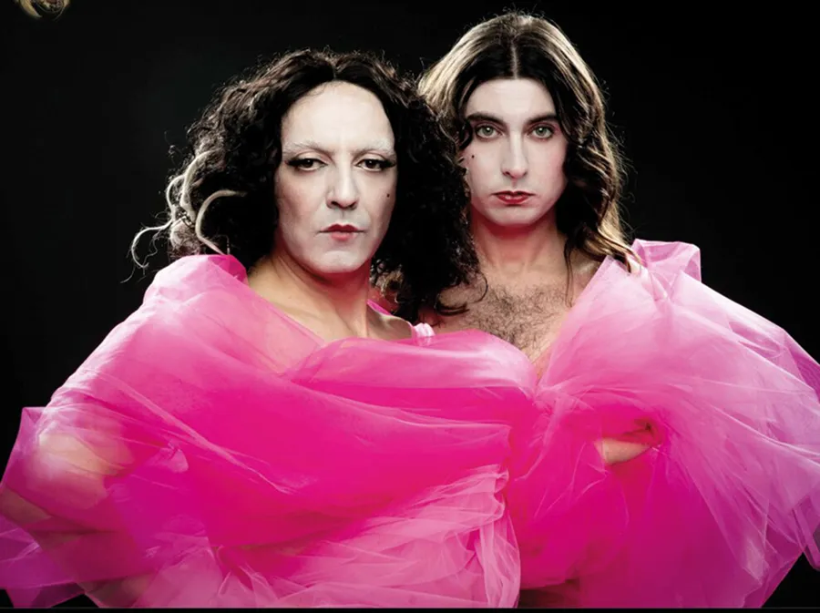 Dos personas posan juntas vestidas con una voluminosa tela de tul de color rosa brillante sobre un fondo negro, evocando el espíritu dramático del «otoño teatral» de Pilar Bardem. Ambas tienen el pelo largo y oscuro, un maquillaje discreto y expresiones serias, con el tul cayendo sobre sus hombros y pechos.