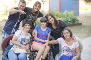 Seis jóvenes integrantes de la asociación El gato de 5 patas, dos de ellos sentados —uno en silla de ruedas—, posan sonrientes en un parque de Rivas