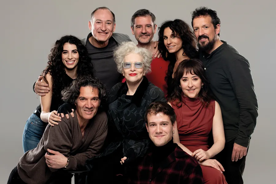 Un grupo de ocho adultos posa muy juntos ante un fondo liso: dos personas sentadas delante y seis de pie detrás de ellas, todas sonriendo a la cámara, en una instantánea que captura un momento de alegría durante la celebración del Otoño Teatral en Pilar Bardem.
