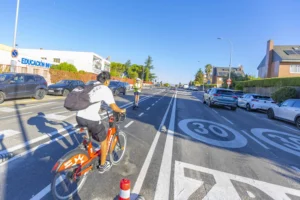 Una persona que circula en una bicicleta de alquiler por un carril bici, seguida por un patinete eléctrico en una calle residencial de Rivas, lo que pone de manifiesto la movilidad urbana local.