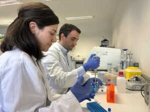 Dos personas con bata y guantes trabajando con micropipetas en un laboratorio