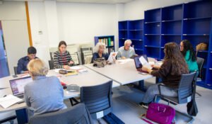 Siete personas del servicio de gestión y resolución de conflictos vecinales trabajan con portátiles y documentos alrededor de dos mesas unidas en una sala luminosa