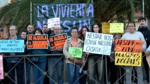 Un grupo de manifestantes se encuentra detrás de una valla metálica en la Ronda de Gloria Fuertes, con pancartas en las que se leen lemas contra los desahucios y los fondos buitre depredadores.