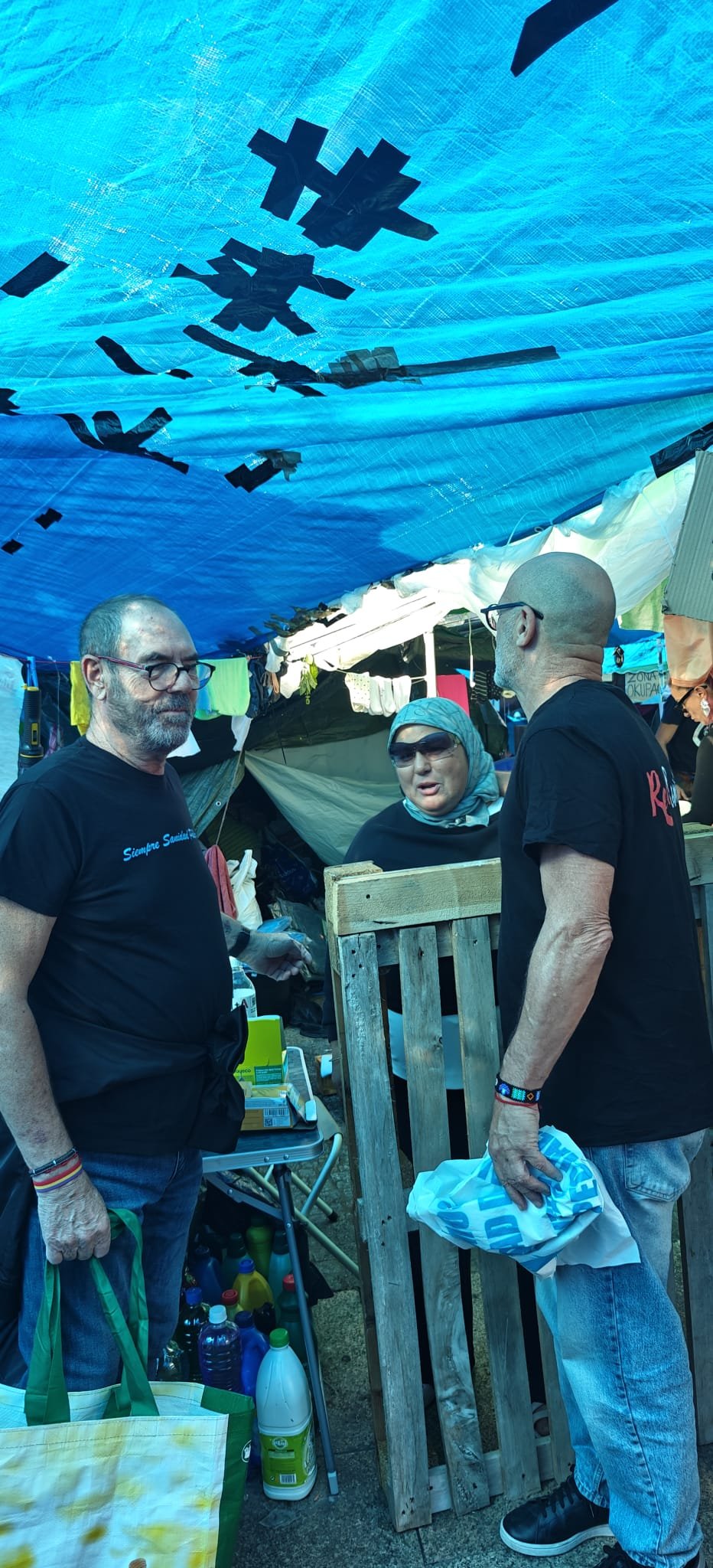 Personas participantes en la acampada, bajo la lona azul del campamento