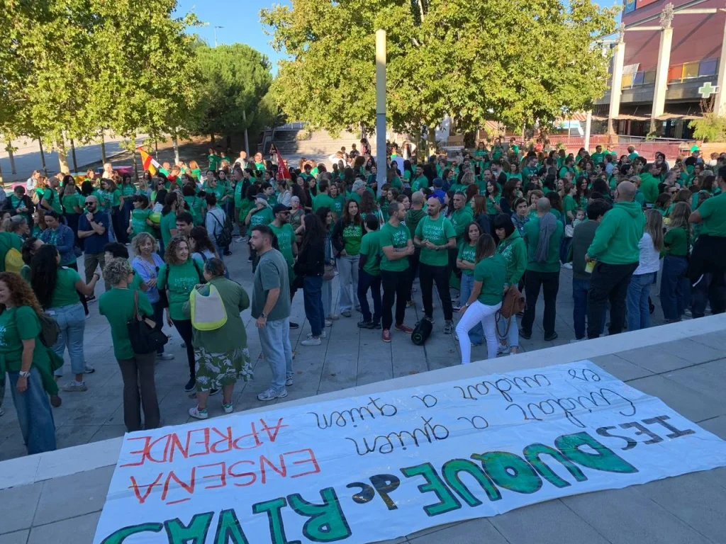 Un numeroso grupo de personas con camisetas verdes, que forman parte de la marea verde, se encuentra en una plaza detrás de una pancarta en la que se lee: IES DUQUE DE RIVAS ENSEÑA A QUIEN CUIDAR A QUIEN APRENDE.