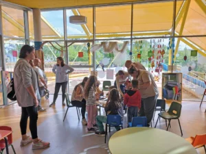 Adultos y niños se reúnen alrededor de una mesa para realizar una actividad artística en un centro comunitario bañado por la luz del sol, participando en las actividades infantiles gratuitas que se organizan en Rivas.