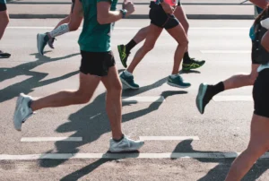 Varios corredores, vestidos con ropa deportiva, corren por una carretera asfaltada durante la Carrera por la Biodiversidad.