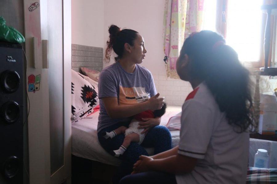 Una mujer con un bebé en brazos conversa con una niña en el interior de una habitación