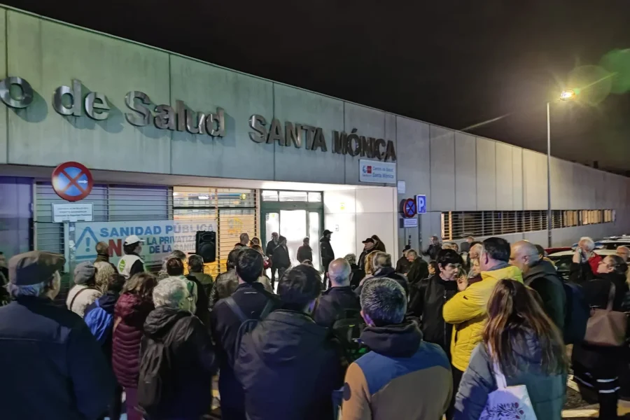 Un grupo se reúne por la noche ante el iluminado Centro de Salud Santa Mónica de Rivas, algunos con pancartas, en señal de manifestación pública en apoyo de la sanidad pública.